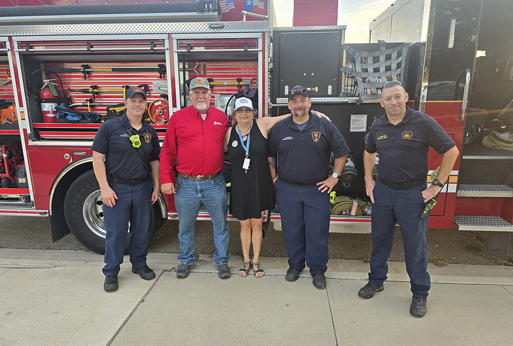 Elisa Roth, Hills of Westwood HOA President, standing with fire department personnel in front of a fire engine at a community event.