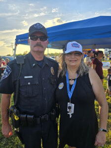 Elisa Roth, Hills of Westwood HOA President, standing with a police officer at an outdoor community event.